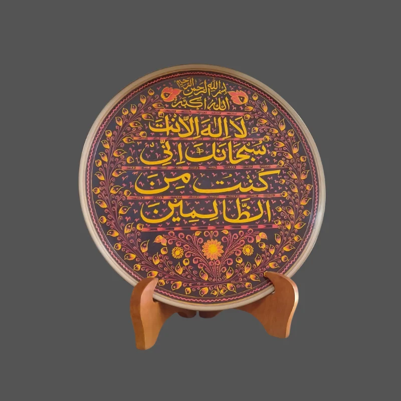 Red and gold display plate with the Kalima written across it, on a wooden stand
