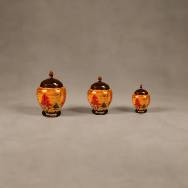 Three graduated lidded wooden jars in amber lac, hand-painted with red and green trees