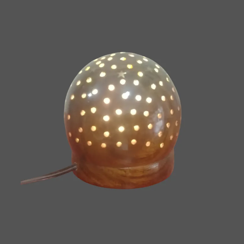 Handcrafted dome-shaped wooden table lamp with a rounded natural wood body and numerous decorative perforations, photographed while illuminated to show its warm ambient light pattern.