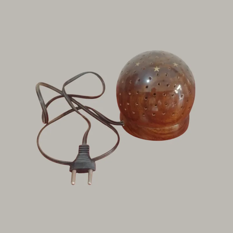 Handcrafted dome-shaped wooden table lamp with a rounded natural wood body and numerous decorative perforations, photographed while illuminated to show its warm ambient light pattern.