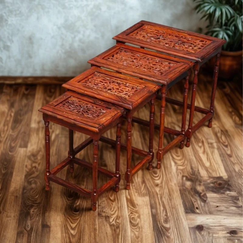 Set of four carved sheesham nesting tables in graduated sizes, stacked one inside the other on a wooden floor
