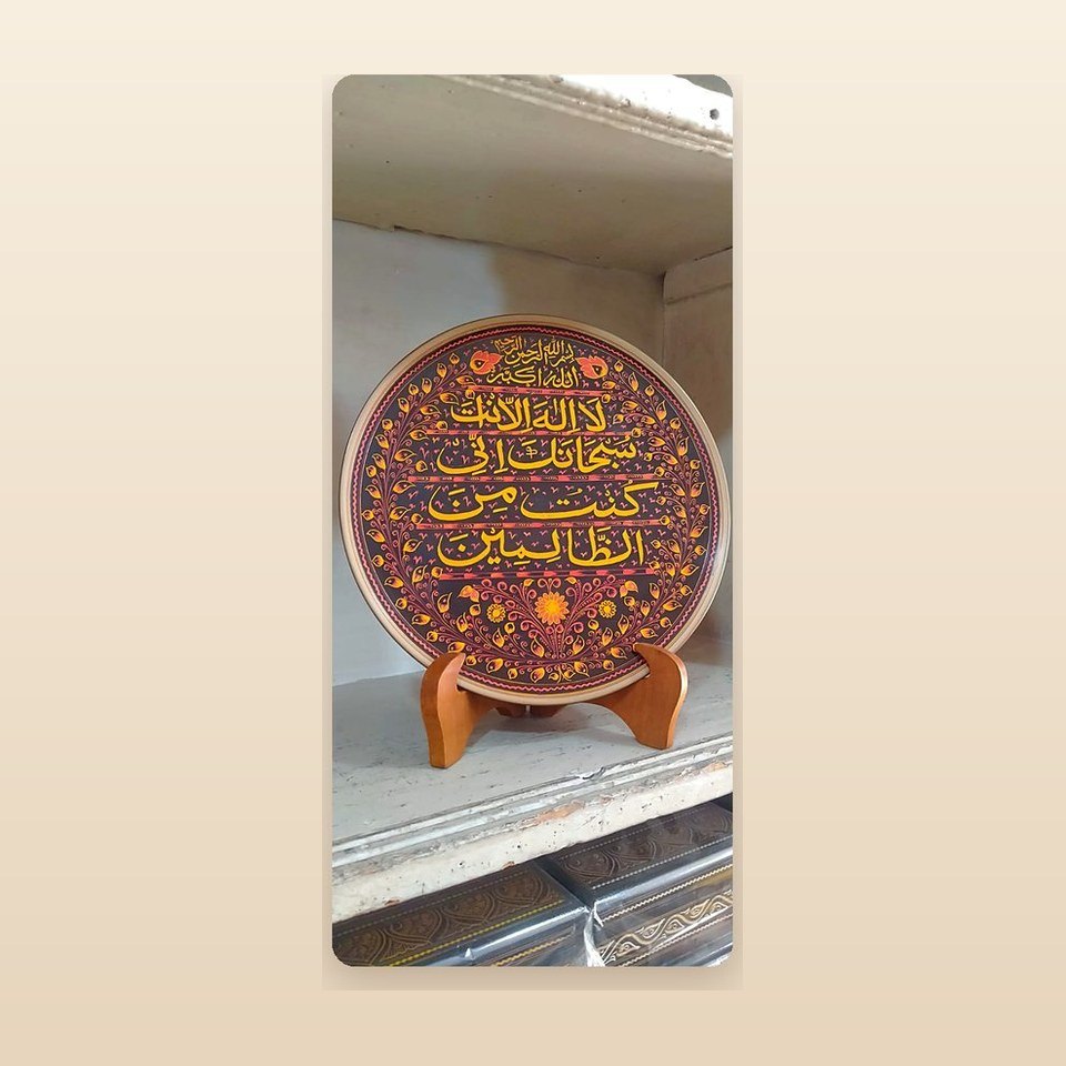 Red and gold display plate with the Kalima written across it, on a wooden stand