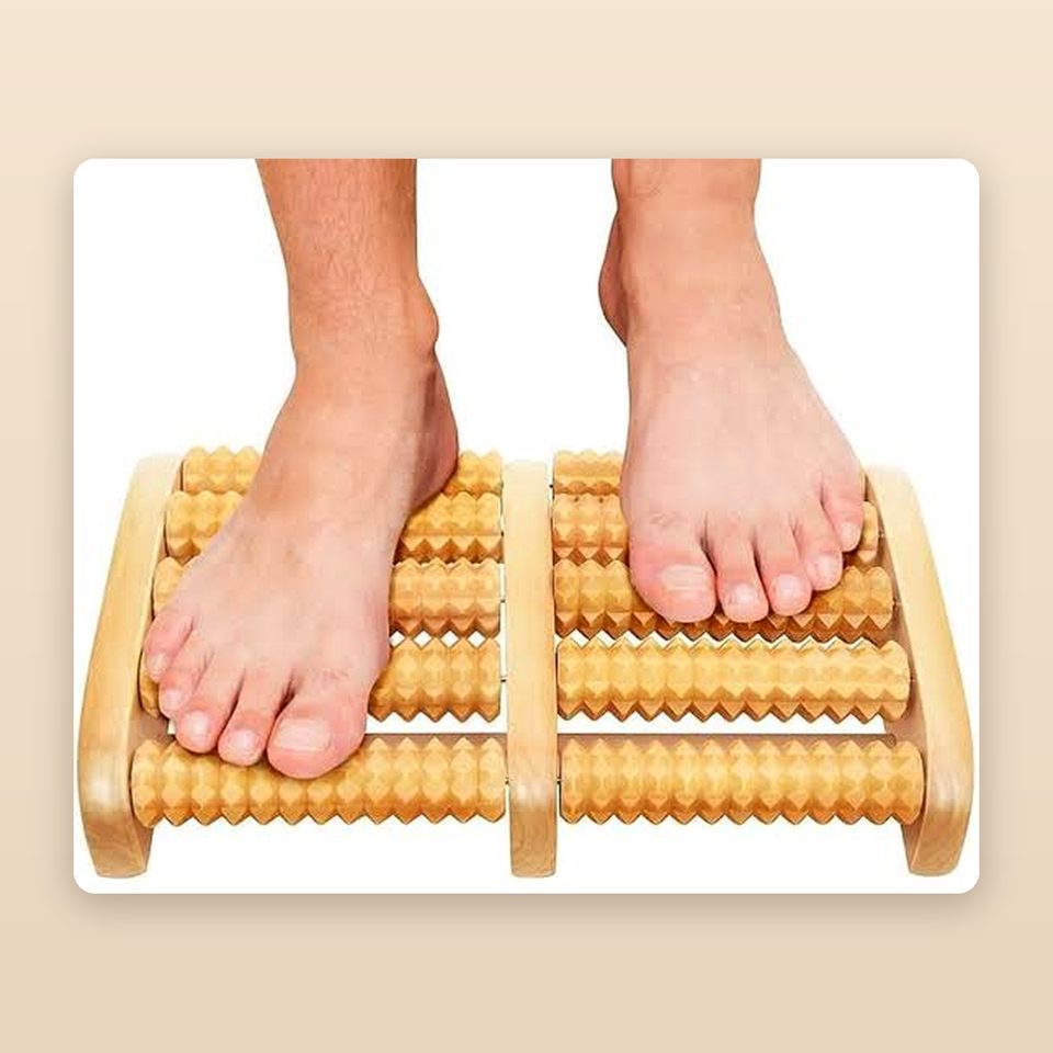 Wooden foot massager with two rows of rollers being used under bare feet